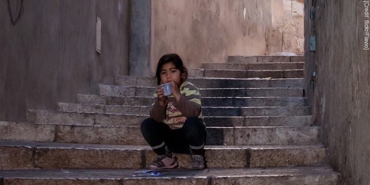 Young girl sipping from a cup while sitting on a brick stairway.