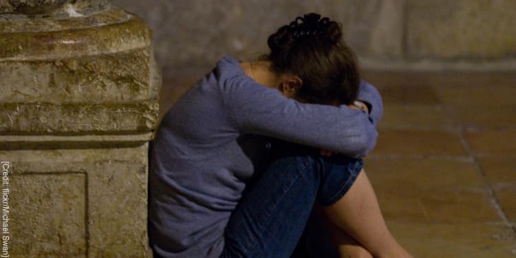 Woman sitting on the ground holding her knees and crying.