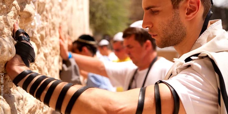 Man with wraps around his arms praying at the Western Wall.