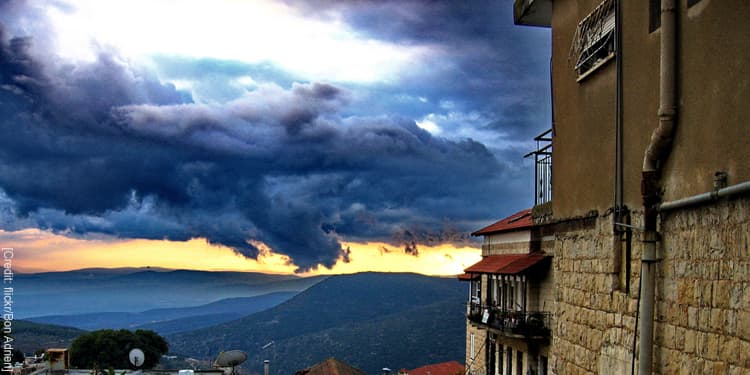 A house that's overlooking hills while dark clouds are overhead.