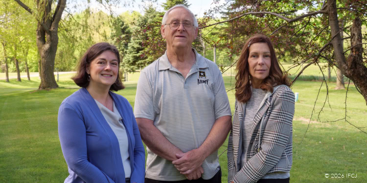 Three individuals sharing a heartfelt moment outdoors, representing donor testimonials for IFCJ, with lush green trees and grass in the background.
