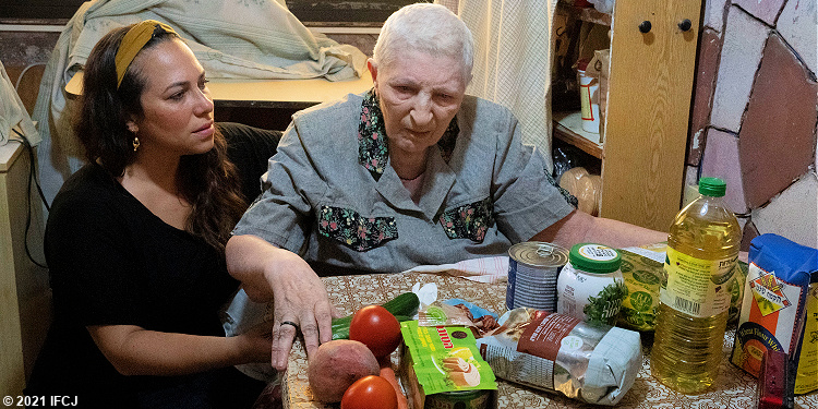 Yael next to elderly Jewish woman sitting at table with food