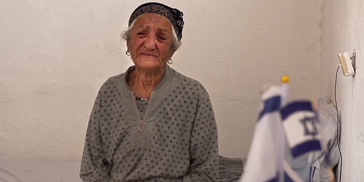 Elderly Jewish woman sitting on a cot crying.