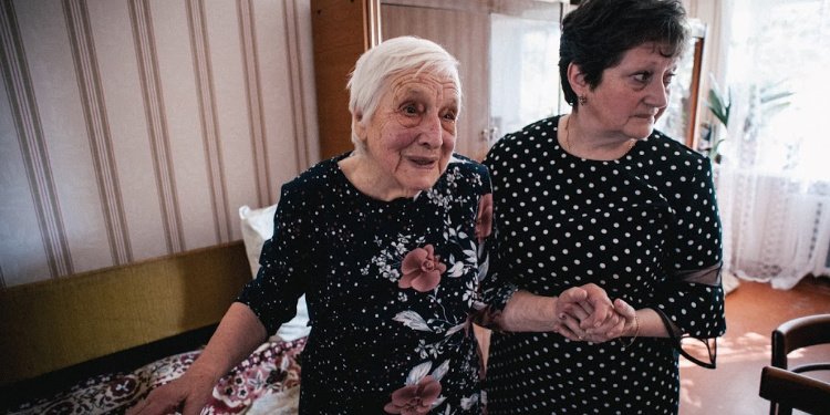 elderly woman, black shirt with flowers, holding hands with homecare worker