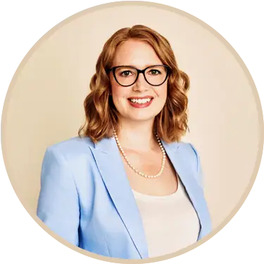 Portrait of Erica Prescott, smiling woman with glasses, wearing a light blue blazer and pearl necklace, against a neutral background.