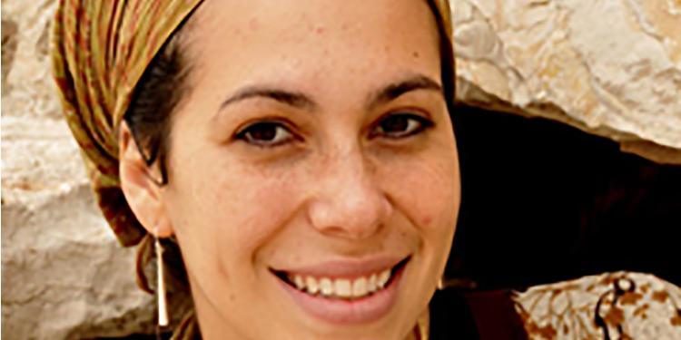 Yael Eckstein smiling as she wears a yellow head scarf and is standing in front of the Western Wall.