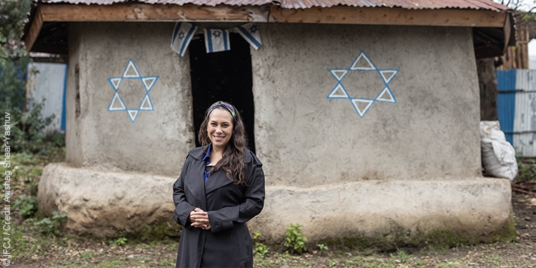 Yael stands outside a mud building with the Star of David painted on the walls.