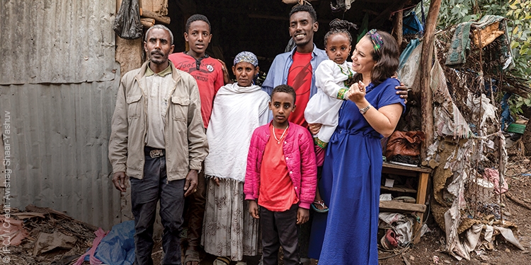 Yael stands with a family outside their home in Ethiopia.