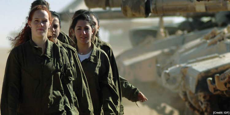 Group of female soldiers walking in a line beside machinery.