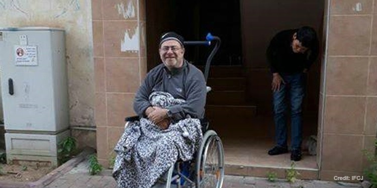 Man in a wheelchair on the sidewalk holding a blanket while smiling.