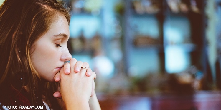 A girl praying with her eyes closed and hands folded.