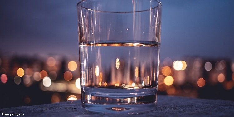 An empty glass sitting on a ledge with a lit up city behind it.
