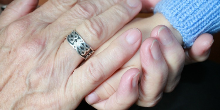 An adult hand with a ring on it holding a small child's hand.