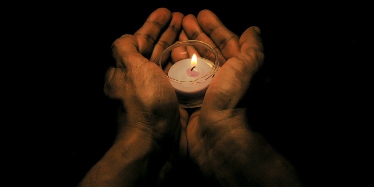 Cupped hands holding a small candle.