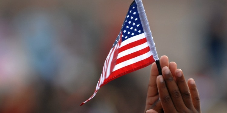 Hands in prayer position while holding a small United States flag.
