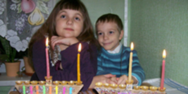 Two children lighting Hanukkah candles together.
