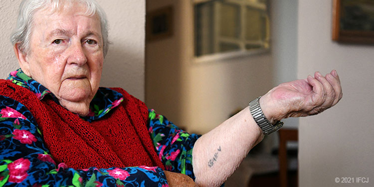 Holocaust survivor, holding arm up with number tattoo on it