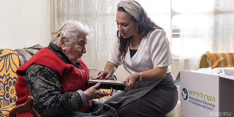 elderly woman sit with Yael Eckstein holding meal kit