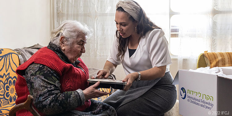 Elderly woman sit with Yael Eckstein holding meal kit