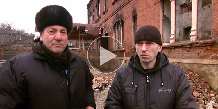 Screenshot of Rabbi Eckstein standing alongside another man in front of a broken-down building.