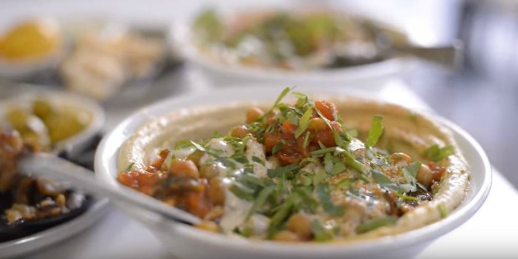 Close up image of hummus with toppings in a white bowl.