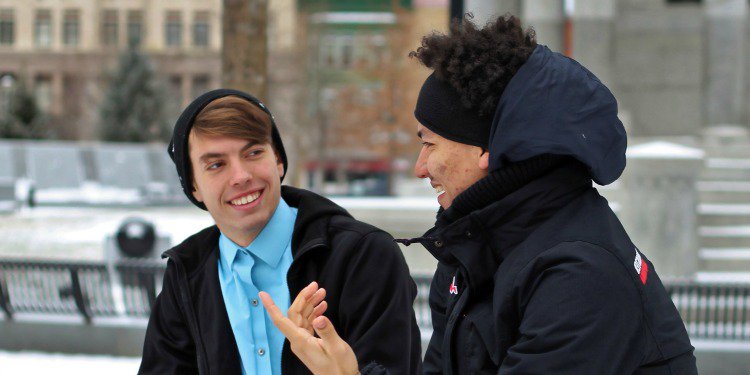 Two men sitting on a bench wearing winter clothing having a conversation