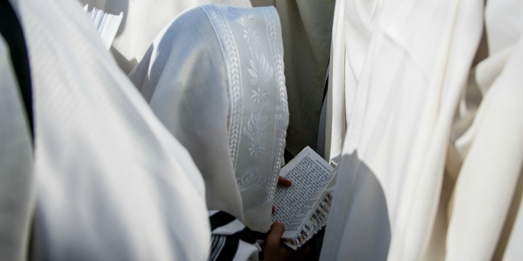 Man in prayer shawl holding a paper in his hands.
