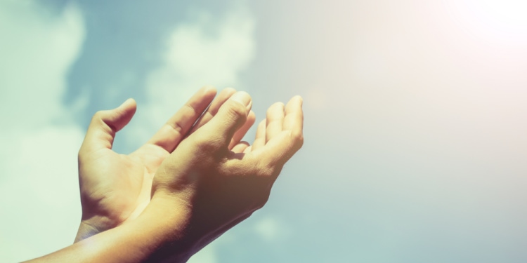 Hands of human praying on blue sky background with sunlight