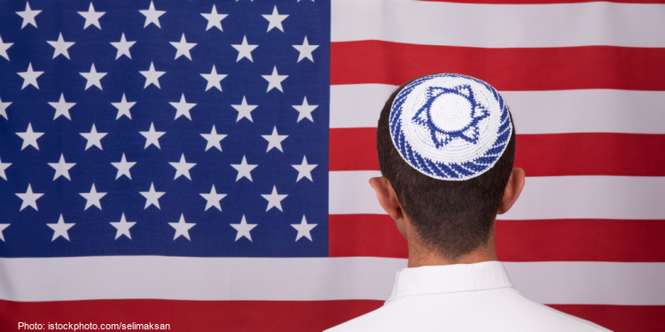 Boy wearing kippah with Israel flag stands in front of flag of United States of America