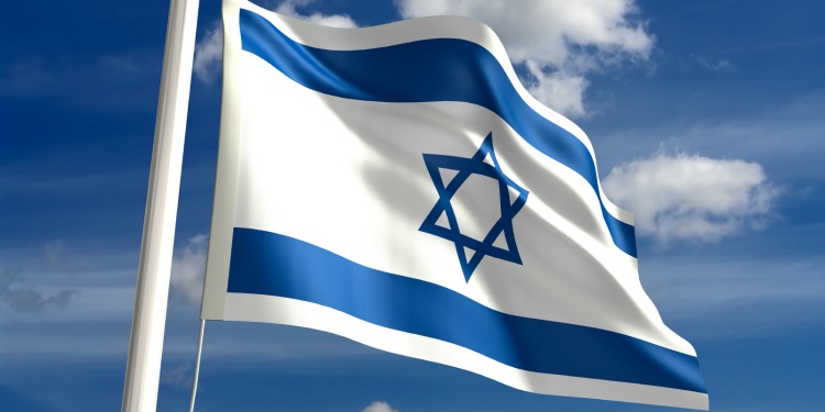 Israeli flag waving in the air against blue cloudy sky.