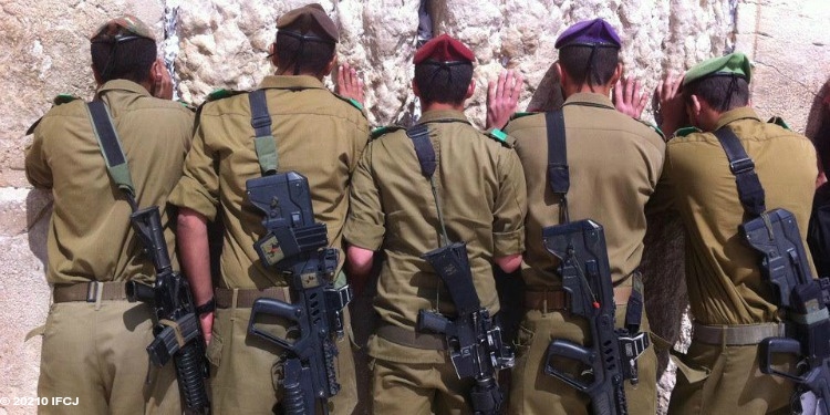 Five soldiers facing the Western Wall praying.