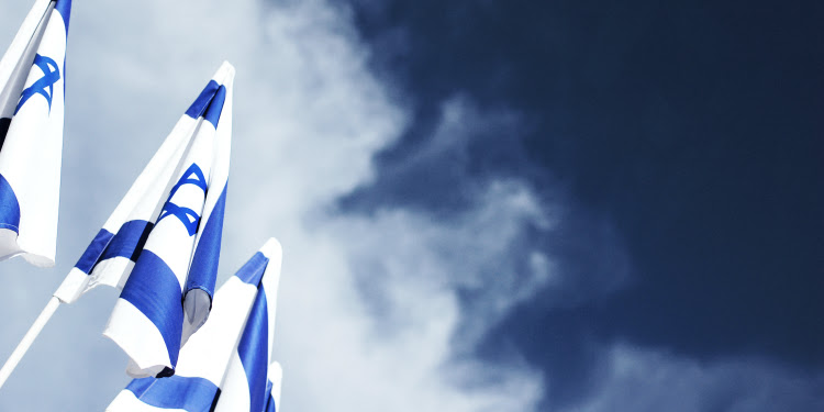 Three Israeli flags with a cloudy blue sky behind them.