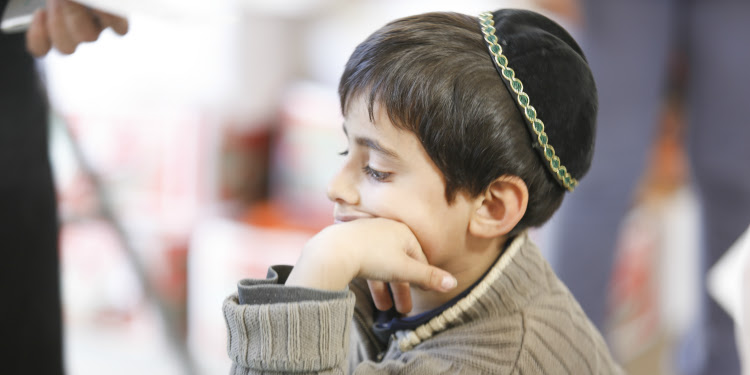 Young boy sitting down with a kippah on.