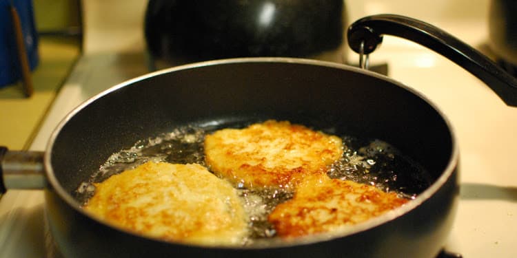 Latkes cooking in oil in a black pan.