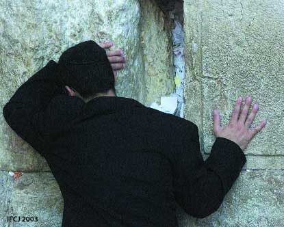 Man in all black praying at the Western Wall.