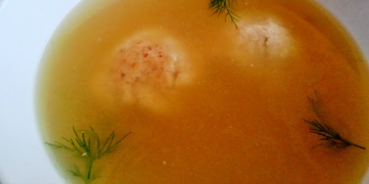 Close up image of matzah ball soup in a white bowl.