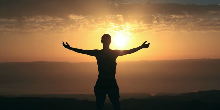 Person stretching their hands out while looking at the sunrise.