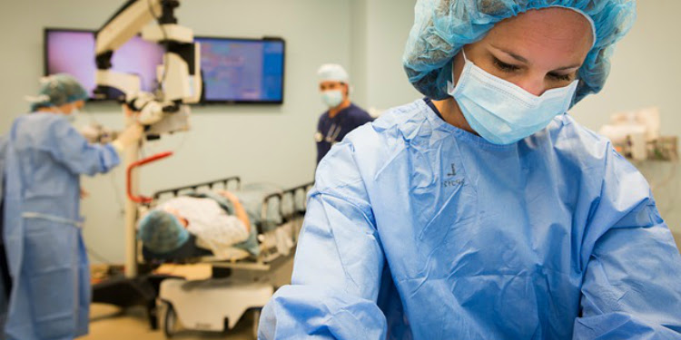 Woman in scrubs looking down while there's medical testing in the background.