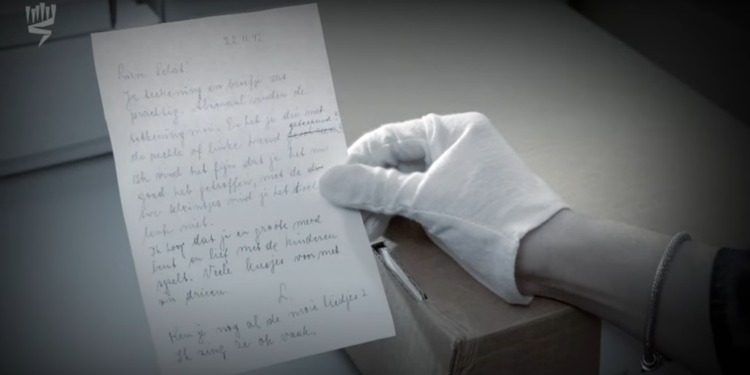 A gloved hand holding a note written in the Holocaust.