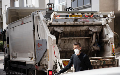 Adult man standing next to garbage truck, wearing face mask
