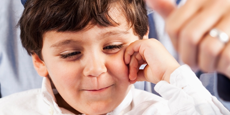 Little boy with his hand on his face while he's looking down smirking.