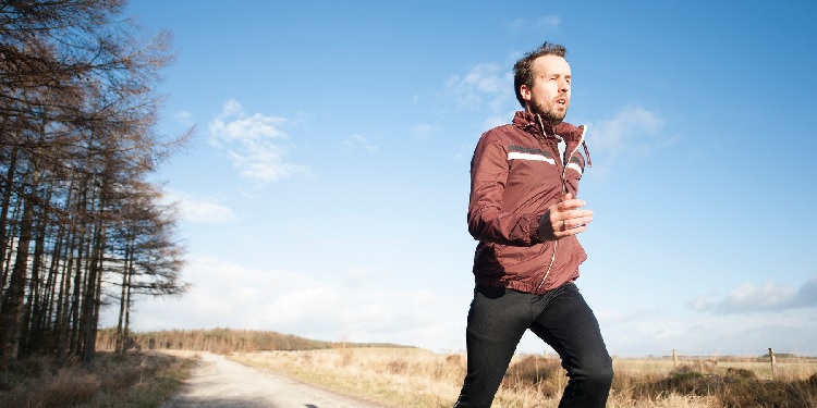 A man in a maroon jacket running through a trail.