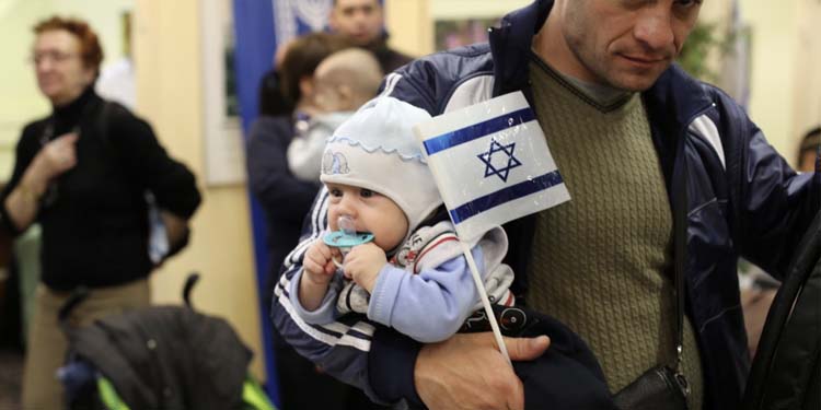 A man holding his newborn while holding a small Israeli flag.