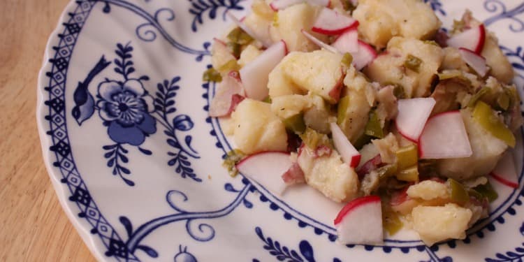 Potato salad with radishes on a blue and white flower patterned plate.