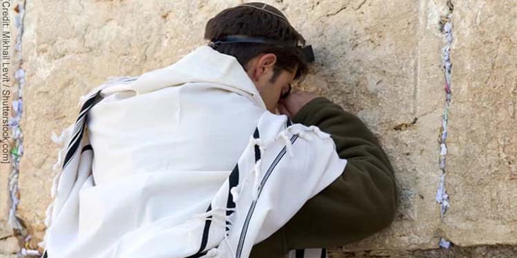 Young man wearing a prayer cloth leaning on the Wester Wall in Jerusalem praying