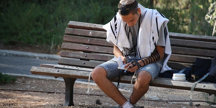 Teenage boy sitting on a wooden bench flipping through a small book.