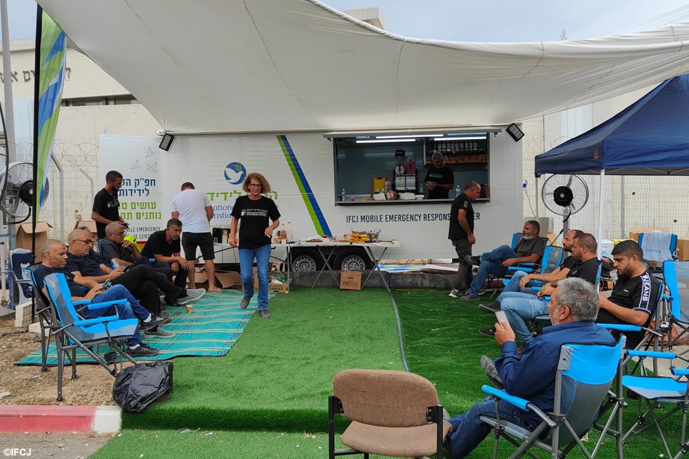 Group of people sit in folding chairs in front of the IFCJ mobile emergency response center at Ramle.