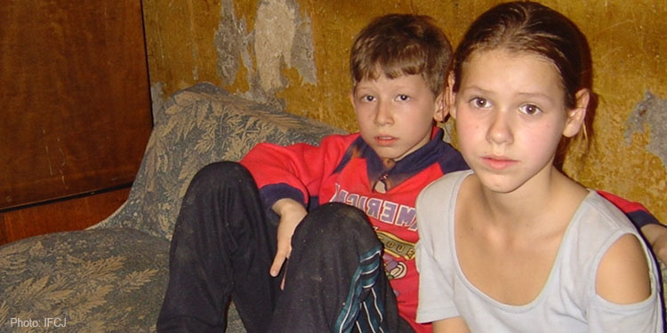 Young boy and girl sit on a ragged mattress