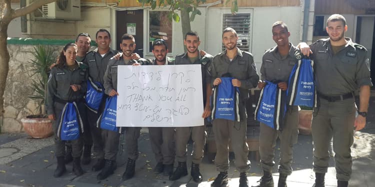 Group of soldiers holding IFCJ branded backpacks while holding up a white sign.