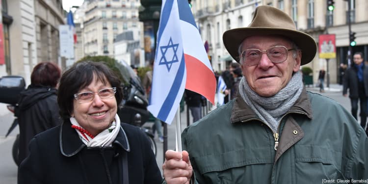 Elderly Jewish couple smiling while holding the Israeli and French flag.
